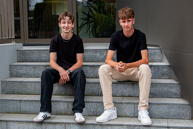 Bild mit den beiden Lernenden, welche nebeneinander vor dem Gebäude sitzen, Swiss Infosec AG